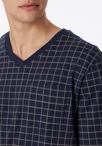 Navy V-neck shirt with white grid pattern, short sleeves, and a front pocket. Made of a soft fabric with a smooth texture.