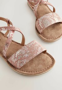 Platta sandaler med korsade remmar i rosa konstläder som har ett reptilmönster. Mjuk fotbädd i beige mocka. Lätt sula med sömdekor.
