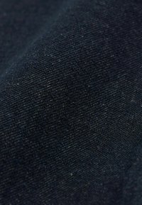 Tmavě modrá denimová látka s jemnou, strukturovanou tkaninou. Povrch vypadá hladce s jemnými barevnými variacemi, které ukazují hluboký námořnický odstín.