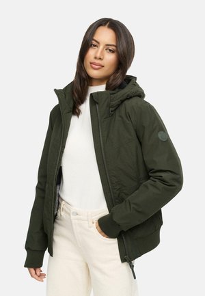 Dark green hooded jacket with a zip front, ribbed cuffs, and patch detail on sleeve. Worn over a white top and cream-colored pants.