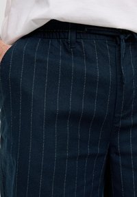 Pantalon bleu marine en coton avec des rayures blanches. Taille élastique avec cordon de serrage. Texture douce, design ajusté et poches latérales.