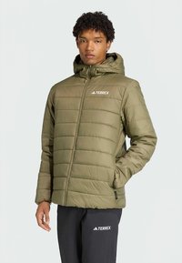 Olive green padded jacket with a hood, featuring quilted sections and a front zipper, displayed with black pants and the Terrex logo.