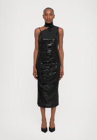 Black sequin dress with a fitted silhouette, asymmetrical neckline, and draped texture. Mid-calf length, paired with black pointed heels.
