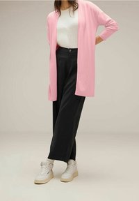 Ljusrosa lång cardigan, vit ribbad topp, svarta vida byxor och vita högskurna sneakers. Mjuk tyg med avslappnad passform.