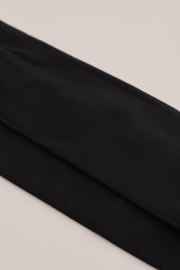 Melna stieptā auduma galvas josla ar mīkstu tekstūru, kārtīgi salocīta, ar gludu virsmu bez rotājumiem.