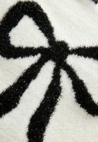 Motif de nœud noir duveteux sur tissu blanc texturé, gros plan montrant des fils doux et scintillants et un fond tricoté.