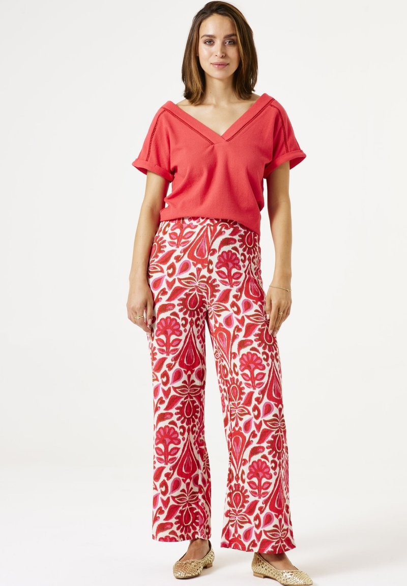 Top corto rojo de manga corta con escote en V combinado con pantalones de pierna ancha que presentan un estampado floral en tonos rosa, rojo y dorado.