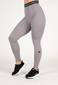 Pilki legginsai su aukštu juodu juosmeniu, kuriame yra "GORILLA WEAR" logotipas ir maža gorilos grafika ant apatinės kojos. Juodi sportiniai batai.