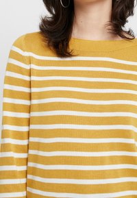 Maglione a righe giallo e bianco. Materiale in maglia morbida, colletto a barca, con righe orizzontali e una vestibilità rilassata.