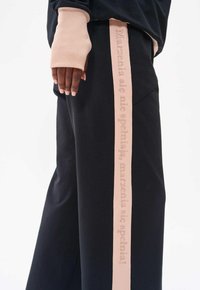 Czarne dresy z szerokim, różowym paskiem bocznym z wytłoczonym tekstem. Rękawy górnej części również wykonane są z podobnego miękkiego różowego materiału.