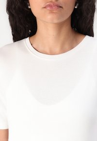 Weißes T-Shirt mit kurzen Ärmeln und rundem Ausschnitt. Glatte Textur und figurbetonte Form. Dezenter Schimmer und leicht transparent in der Mitte.