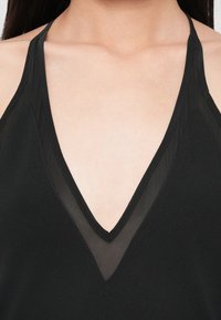 Μαύρο αμάνικο τοπ με βαθιά V-λαιμόκοψη, διαφανείς λεπτομέρειες και αντίθετες υφές στους ώμους και τη λαιμόκοψη.