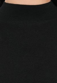 Detailní záběr na černý pletený svetr s ribbaným vysokým límcem.