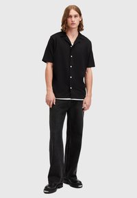 Black short-sleeve shirt with a soft texture, featuring a camp collar and white buttons, paired with flared black jeans and chunky black boots.