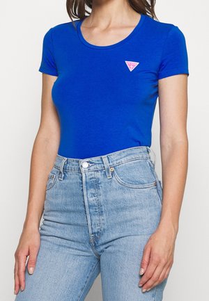 Kongeviolet tætsiddende t-shirt med rund hals, korte ærmer og en lille lyserød trekantet logo på venstre bryst. Kombineret med lyse denimjeans.