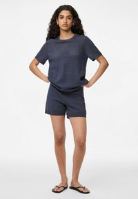 Ensemble haut en tricot texturé bleu marine et shorts avec ourlet festonné. Tissu léger, manches courtes et coupe décontractée, complété par des tongs simples.