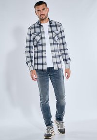 Karierte Flanellhemden in Grau, Weiß und Schwarz, mit zwei Brusttaschen. Getragen über einem weißen T-Shirt und kombiniert mit verwaschenen blauen Jeans und Turnschuhen.