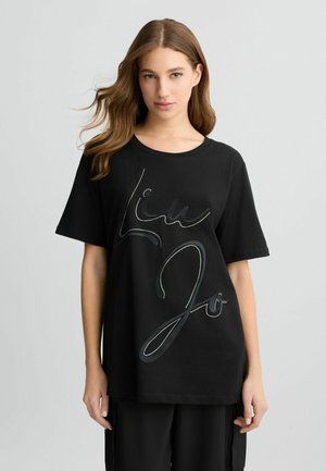 T-shirt en coton noir avec un grand logo en cursive argenté sur le devant. Manches courtes et coupe décontractée. Texture lisse.