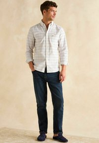 Košeľa na gombíky s jemným kockovaným vzorom v bielej, modrej a červenej farbe, kombinovaná s tmavomodrými džínsami a námorníckymi nazúvacími topánkami. Jednoduchý dizajn.