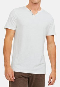 Weißes Kurzarm-T-Shirt mit V-Ausschnitt und zwei Knopf-Akzenten. Hergestellt aus weichem Stoff, mit einer glatten Textur und einem lockeren Sitz.