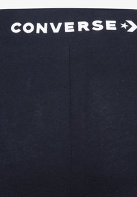 Marineblå leggings med en glatt tekstur og elastisk midje. "CONVERSE" logo trykt i hvitt på toppen. Enkel, tettsittende design.
