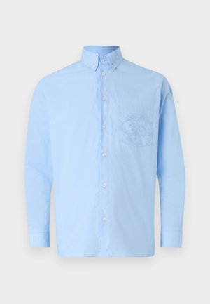 Camisa de botones de manga larga de color azul claro, hecha de algodón, con un bolsillo frontal que presenta un diseño gráfico detallado. Textura suave con un cuello estándar.