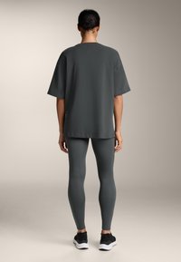 Tricou oversized gri închis cu guler rotund, asortat cu colanți gri închis și pantofi sport negri. Textură netedă, croială lejeră.