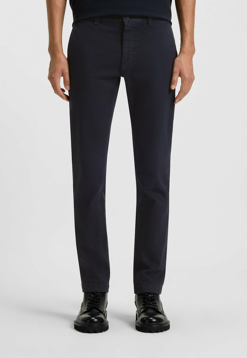 Pantalones de algodón azul marino con corte de pierna recta; con cinturillas, bolsillos frontales y una textura suave. Combinados con botas negras de cordones.