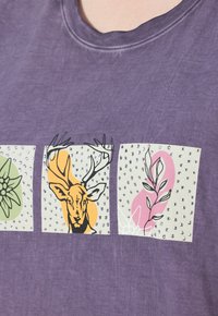 Camiseta de algodón morada con tres cuadrados estampados: ilustración de ciervo, diseño floral y forma abstracta de planta con strass.
