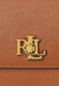 Geantă din piele maro texturată, cu un închizător aurie în formă de logo "RL", având un finisaj neted și un model de fibră distinct pe suprafață.