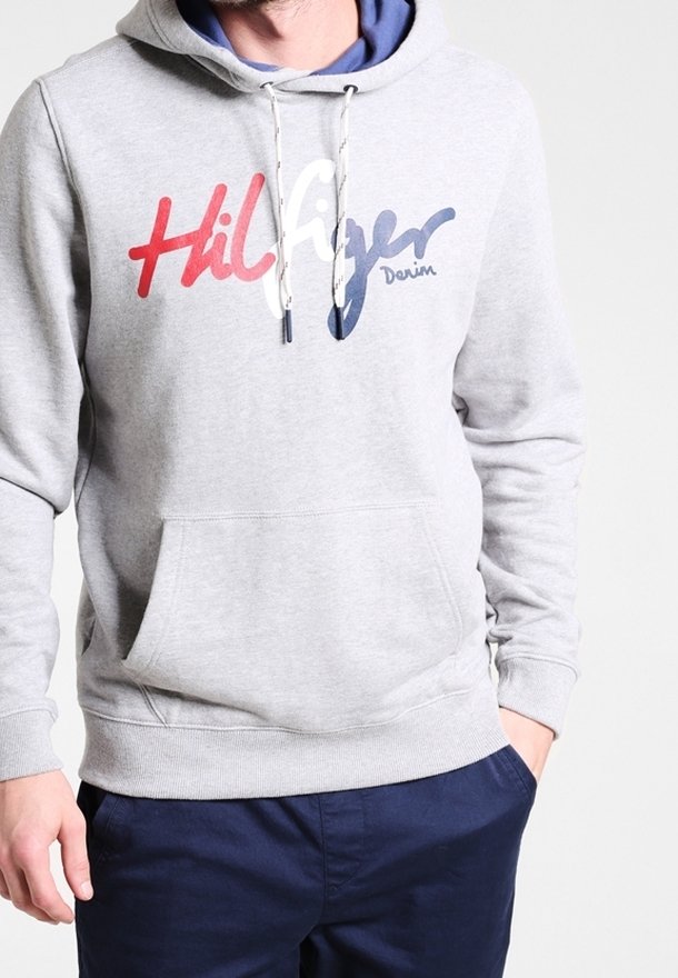 Felpa grigia con tasca frontale, cappuccio con lacci e logo stampato "Hilfiger Denim" in rosso, bianco e blu. Materiale jersey morbido.