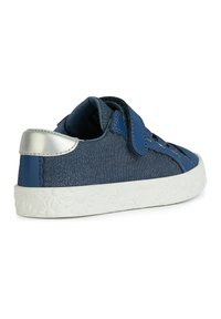 Zapatilla azul con textura de mezclilla, acentos plateados y suela blanca con un patrón floral. Cinta de velcro y detalles de cordones en la parte superior.