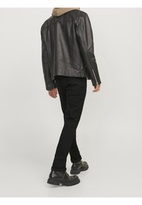 Giacca di pelle nera con una texture liscia, vestibilità su misura e dettagli sulle spalle, abbinata a jeans neri e stivali neri chunky.