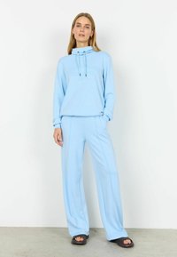 Trening bleu deschis, realizat din țesătură moale. Hanorac cu glugă și șnururi, și pantaloni largi cu cusături laterale. Textură netedă.