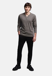Camisa henley gris de manga larga con rayas texturizadas, combinada con pantalones negros y zapatos negros de cordones. El modelo está de pie contra un fondo sencillo.