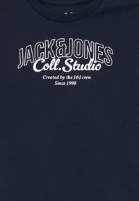 Mörkblå bomulls-t-shirt med ett vitt grafiskt tryck som säger "JACK & JONES Coll. Studio" och inkluderar varumärkesdetaljer.