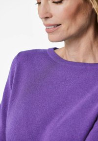 Lila gestrickter Pullover mit Rundhalsausschnitt und glatter Textur, die Nahaufnahmen der feinen Webart des Stoffes zeigt.