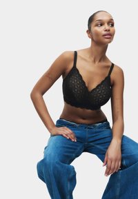 Soutien-gorge bralette en dentelle noire avec un motif triangulaire, des bords festonnés, des bretelles ajustables et une texture lisse. Associé à un jean en denim bleu ample.
