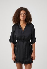 Robe en satin noir à manches courtes, avec une finition en dentelle aux extrémités et à l'ourlet, nouée à la taille avec une ceinture assortie.