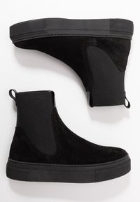 Botines de ante negro con paneles elásticos en los laterales, suelas de goma texturizada y tiradores en la parte posterior para ponerlos y quitarlos fácilmente.