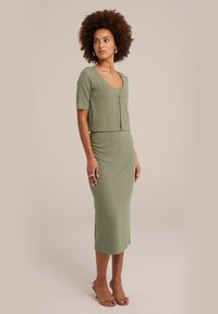 Olivgrön ribbad klänning med figurnära design, korta ärmar och v-ringning, med en diskret knappdetalj framtill.