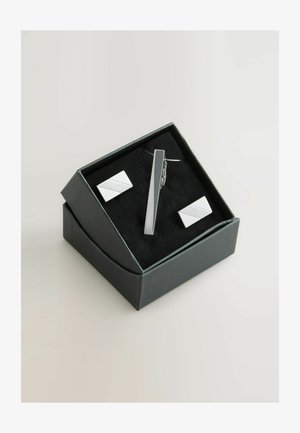 Srebrna kravata i pravokutne manšete s dijagonalnim urezom, smješteni u crnu kutiju s mekanim unutarnjim oblogom.