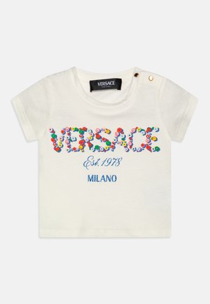 Balts kokvilnas T-krekls ar krāsainiem ziedu izšuvumiem, kuros ir vārdi "VERSACE", "Est. 1978" un "MILANO", ar zelta pogas detaļu uz pleca.