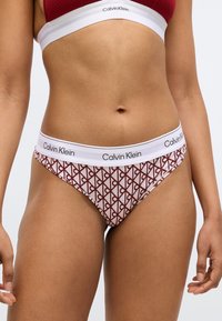 Bikiny Calvin Klein s potlačou, s bielym pásom s logom, geometrickým červeno-krémovým vzorom a jemnou bavlnenou textúrou.