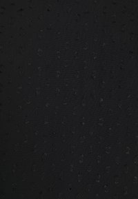 Svart texturerat tyg med små, upphöjda prickar över hela ytan som ger ett subtilt mönster och variation i ytdjup.