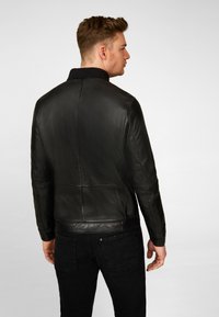 Black leather jacket with a smooth texture, featuring a high collar and seam detailing on the back. Worn with black jeans.