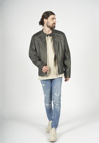 Grå läderjacka med kviltade axlar, framdragkedja och två fickor med dragkedja; bärs över en beige skjorta och slitna blå jeans.