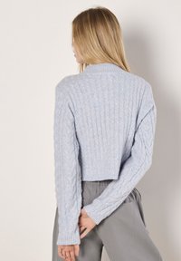 Jasnoniebieski krótki sweter z teksturowanym wzorem w warkocze, ściągaczami przy mankietach i prostym okrągłym dekoltem. Miękka, dziana tkanina.