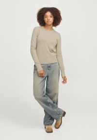 Beiger langärmliger Pullover mit Rundhalsausschnitt, kombiniert mit hellblauen hochtaillierten Jeans und braunen Knöchelstiefeln. Einfaches, tailliertes Design.