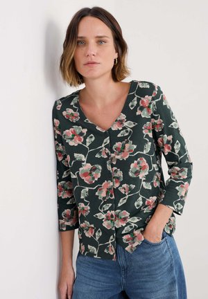 Chemisier floral vert foncé à manches trois-quarts. Orné de motifs de fleurs roses et blanches. Tissu doux, coupe décontractée, à associer avec un jean.